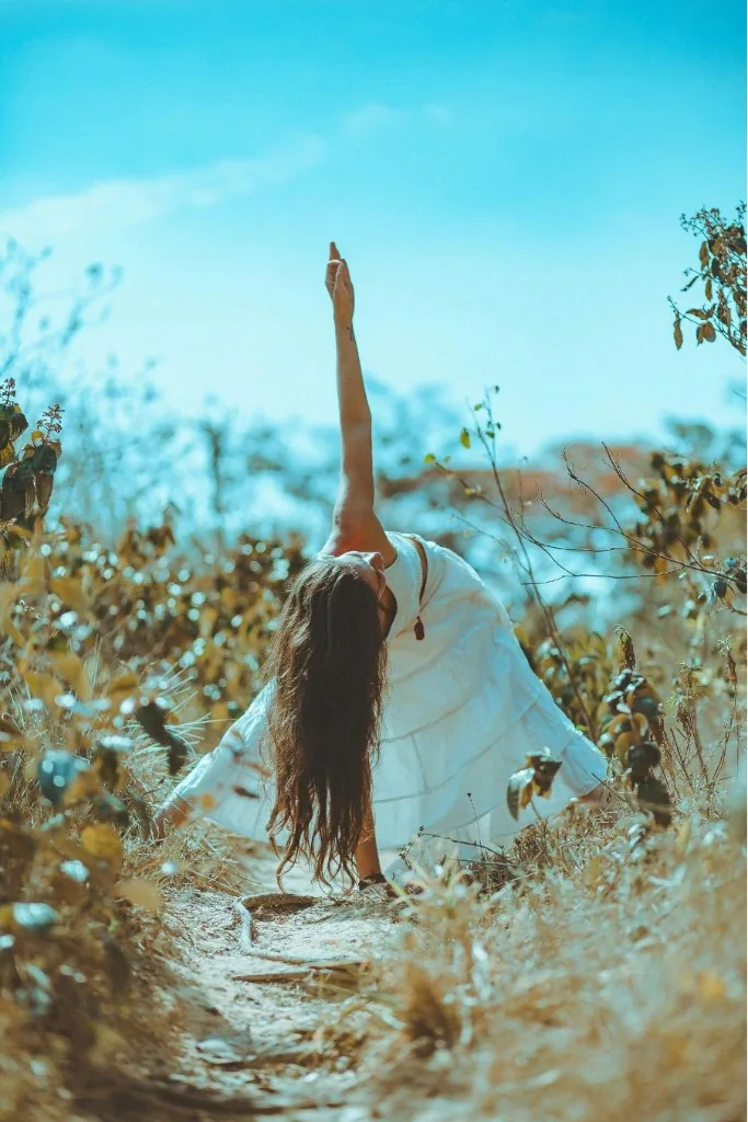 Liis Ugandi in a side bend outdoors in dry grass, white dress, blue sky. Goyoga Tallinn.