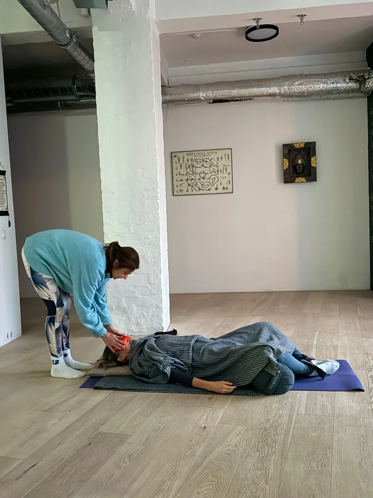 Liis Ugandi adjusting a student lying down with an eye pillow at Goyoga Tallinn.
